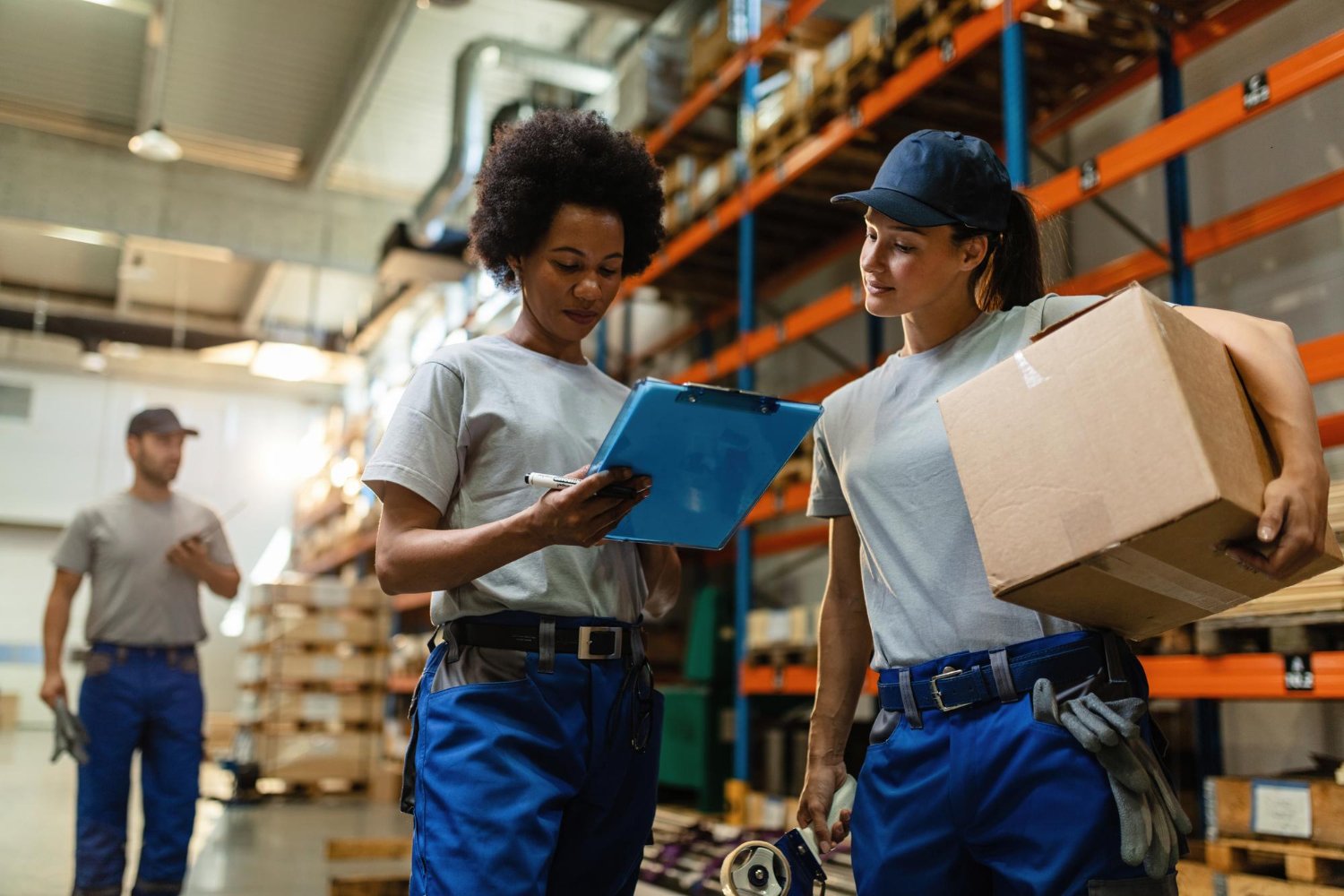 Logística reversa no mercado de trabalho: Duas jovens em um armazém, uma segurando uma prancheta e a outra olhando para ela, cercadas por prateleiras e armazenamento.