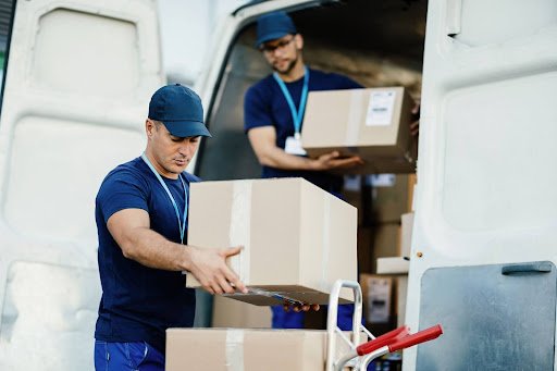 Logística reversa gestão empresarial: Dois entregadores em uniformes azuis carregando caixas em uma van.