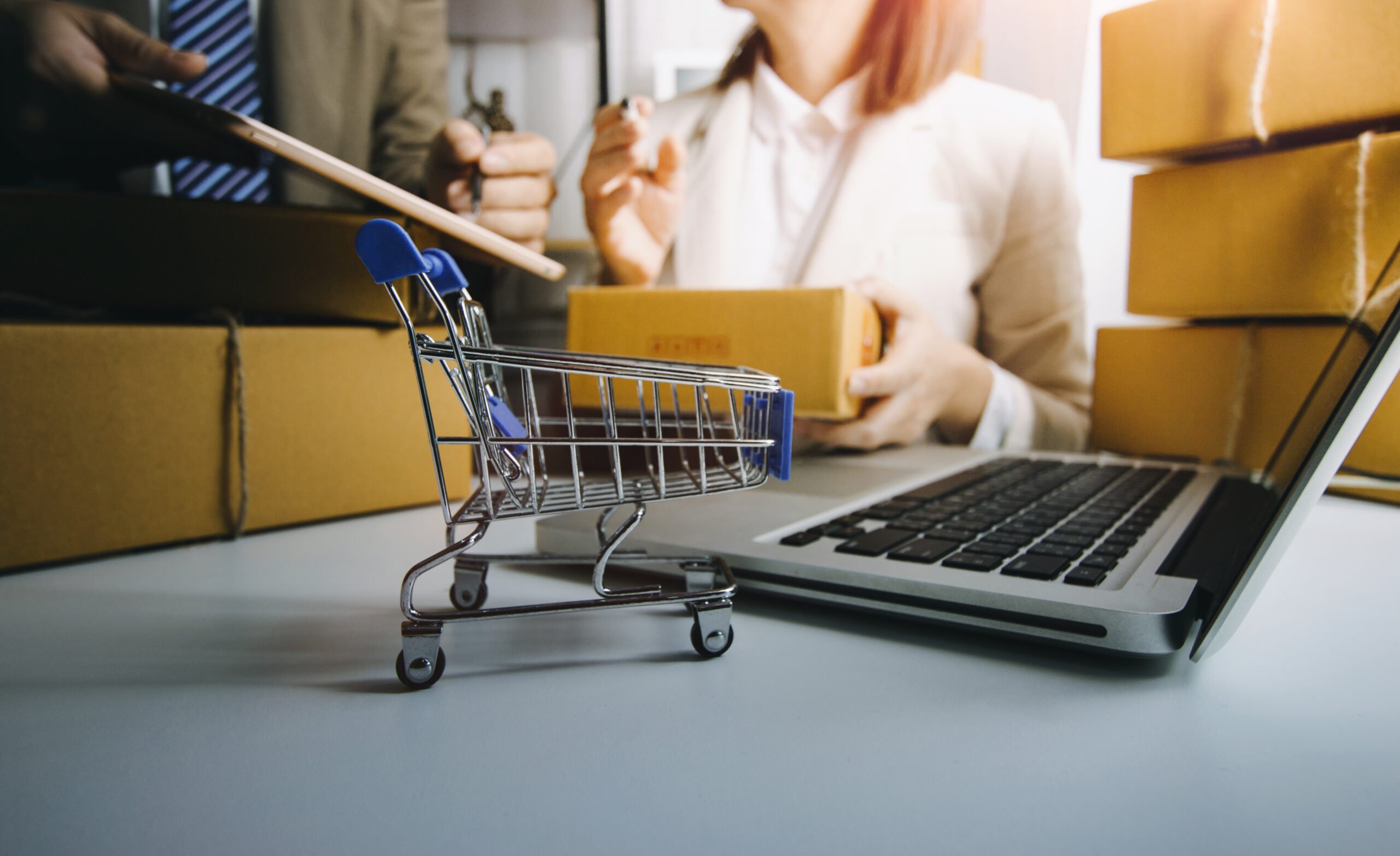 Logística Reversa no varejo e no e-commerce: Uma jovem com cabelo longo e vermelho trabalhando em um laptop, com um pequeno carrinho de compras em primeiro plano sobre a mesa.