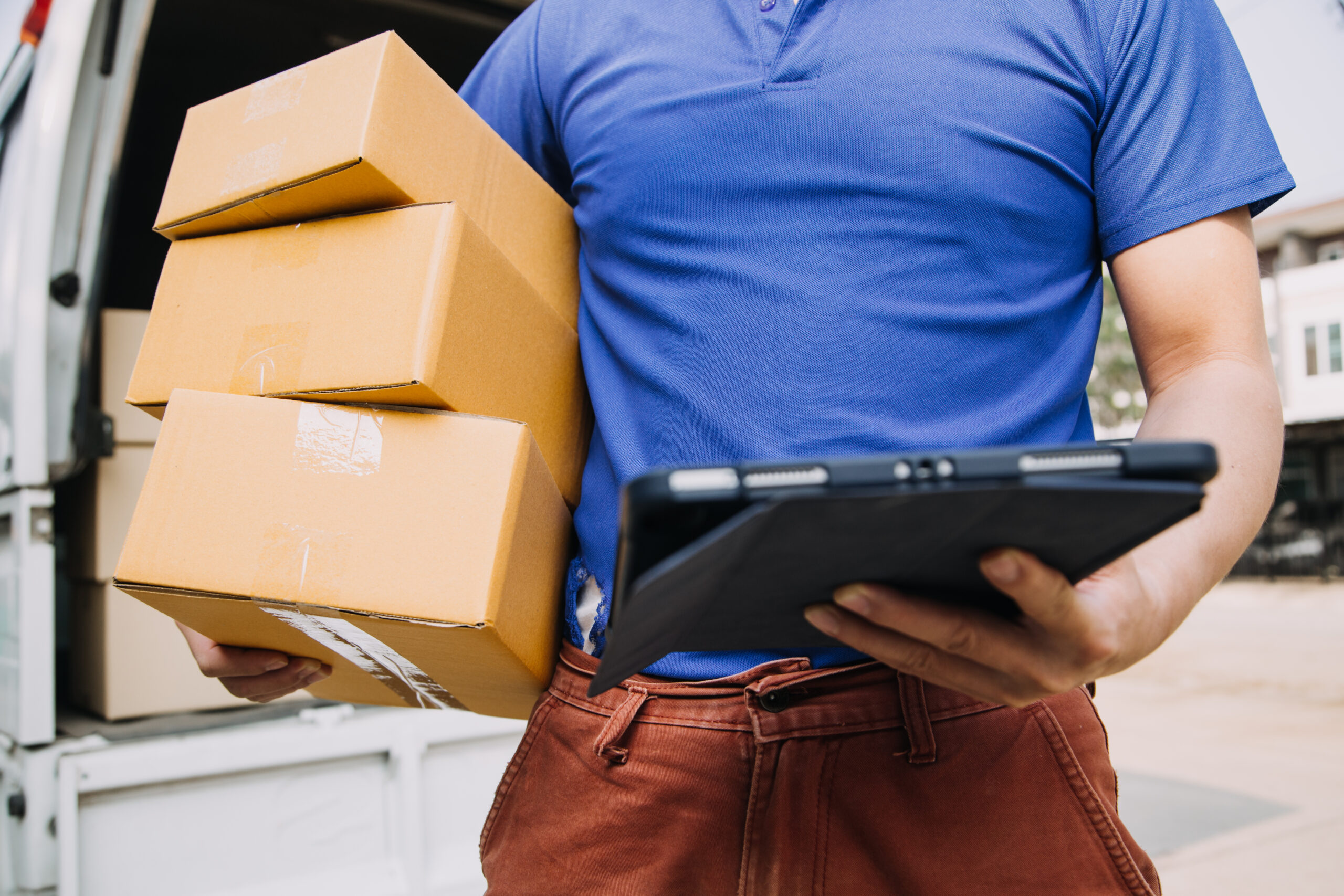 Inovação em Logística Reversa: Um homem vestido com uma camisa azul e calças marrons, segurando um tablet, cercado por caixas de papelão.